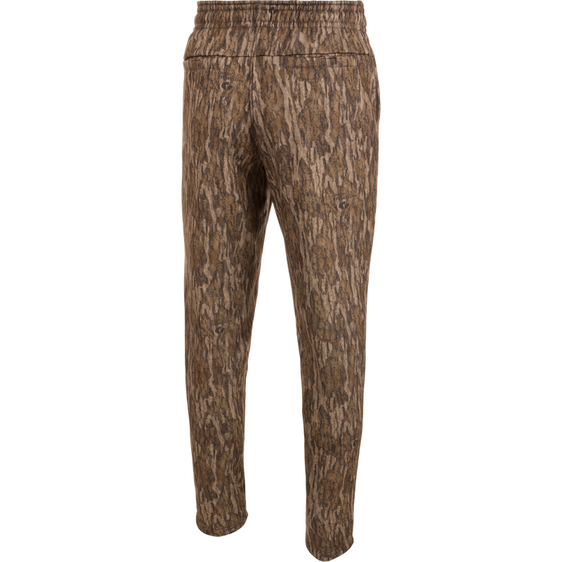 Drake Under-Wader Jogger, camouflage pants with tree pattern, designed for warmth, comfort, and durability under waders, featuring tapered legs, elastic waist, and multiple pockets.