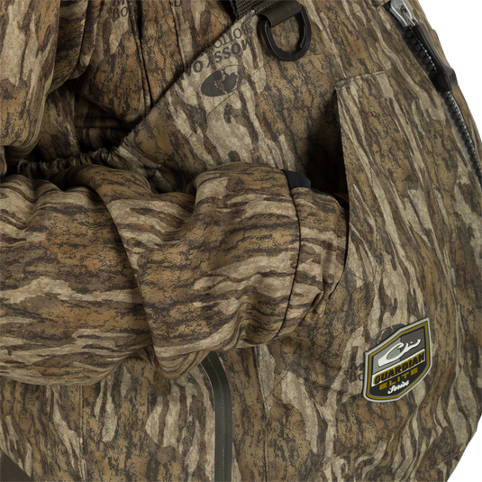 Uninsulated Guardian Elite HND Front Zip Wader - Original Treestand: A person wearing a camouflage jacket with a logo, standing in the marsh, showcasing the waterproof front zipper and durable construction of the wader.