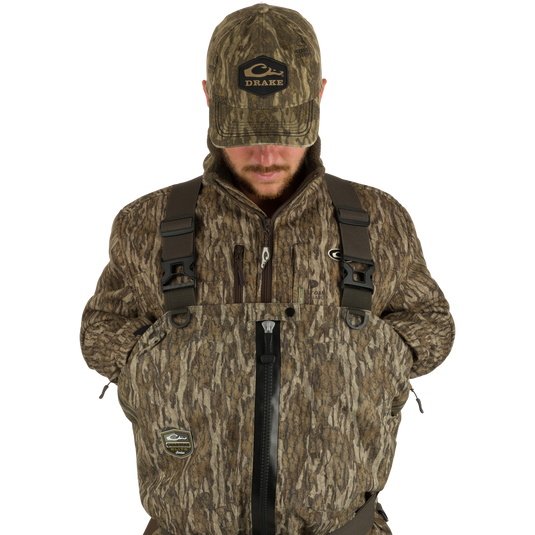 Uninsulated Guardian Elite HND Front Zip Wader - Original Treestand: A man in a camouflage outfit wearing the Guardian Elite HND Front Zip Wader, featuring X-Crossing-Back Shoulder Straps, Magnattach™ front call pockets, and a waterproof front zipper.