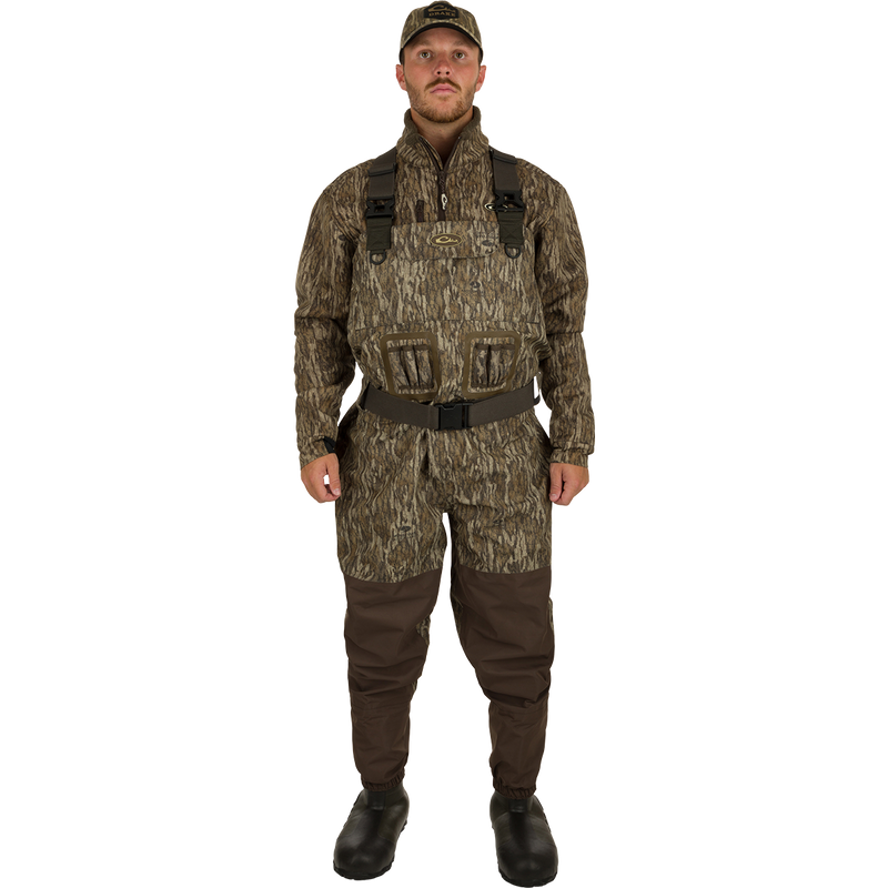 A man in camouflage waders, hat, and boots, showcasing the Insulated Guardian Elite Vanguard Breathable Waders by Drake Waterfowl for hunting.