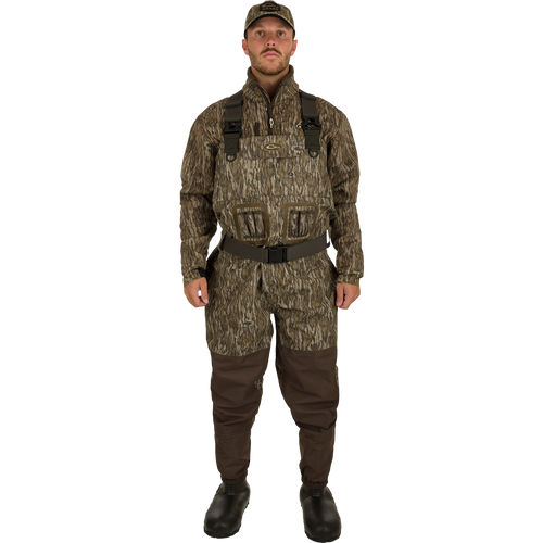 A man in camouflage waders, hat, and boots, showcasing the Insulated Guardian Elite Vanguard Breathable Waders by Drake Waterfowl for hunting.