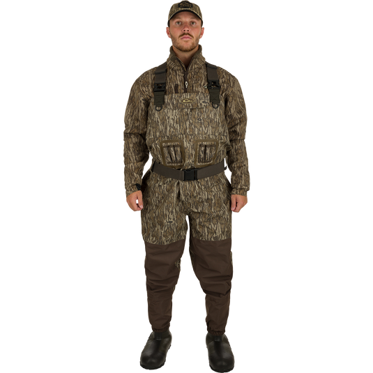 A man in camouflage waders, hat, and boots, showcasing the Insulated Guardian Elite Vanguard Breathable Waders by Drake Waterfowl for hunting.