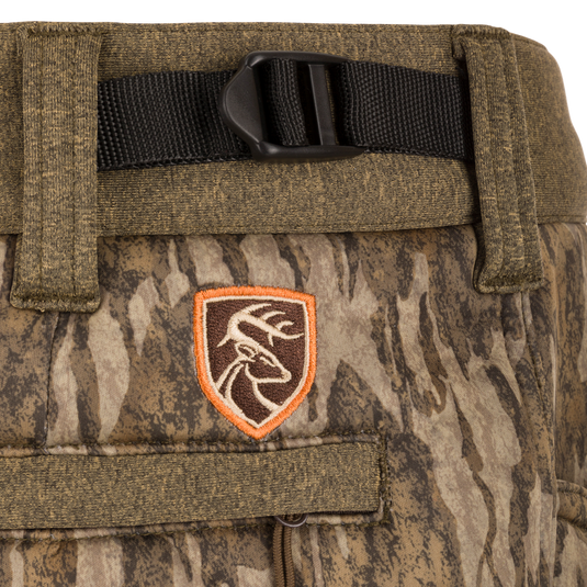 Close-up of Youth Silencer Pant with Agion Active XL, showing camouflage fabric, front slash pockets, adjustable waist, and black strap detail.