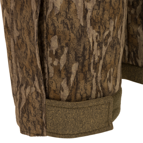 Close-up of the Silencer Bib, featuring camouflage fabric with vertical pockets and lanyards for hunting gear.