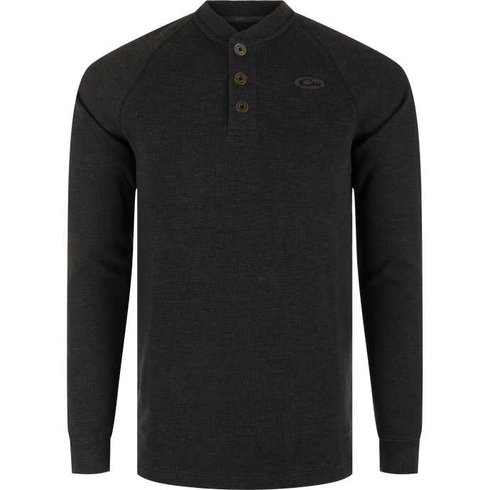 A black long sleeve Henley shirt with metal logo buttons, raglan sleeves, rib knit collar, and cuffs. Made of waffle mélange fabric for comfort, antimicrobial, and moisture-wicking properties. Split tail hem for versatile styling.