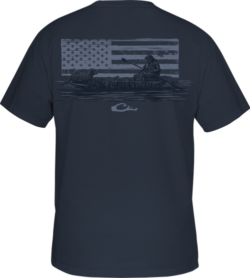 Kayak Flag T-Shirt featuring a graphic of a man in a boat with dogs, overlaying an American flag, and a Drake logo on the front pocket.