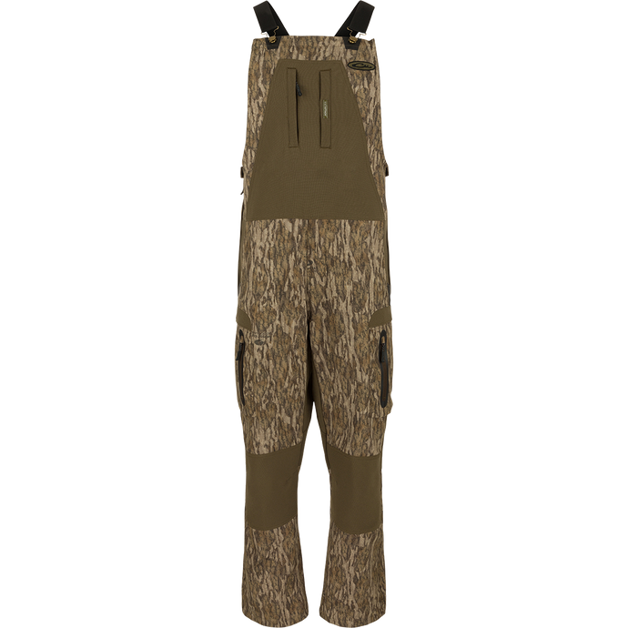 MST Tech Stretch Bibs with camouflage pattern, featuring elastic shoulder straps, multiple zippered pockets, and reinforced knees and seat for hunting and outdoor activities.