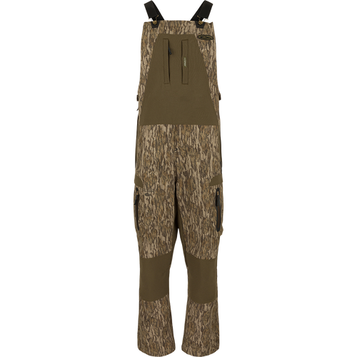 MST Tech Stretch Bibs with camouflage pattern, featuring elastic shoulder straps, multiple zippered pockets, and reinforced knees and seat for hunting and outdoor activities.