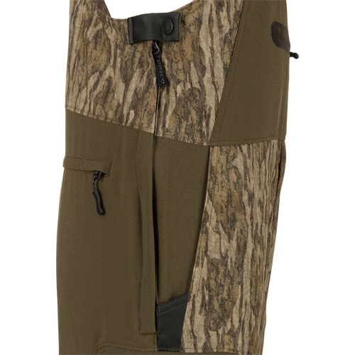 MST Tech Stretch Bibs with camouflage pattern, featuring front slash pockets, zippered leg pockets, and reinforced knees for hunting activities.