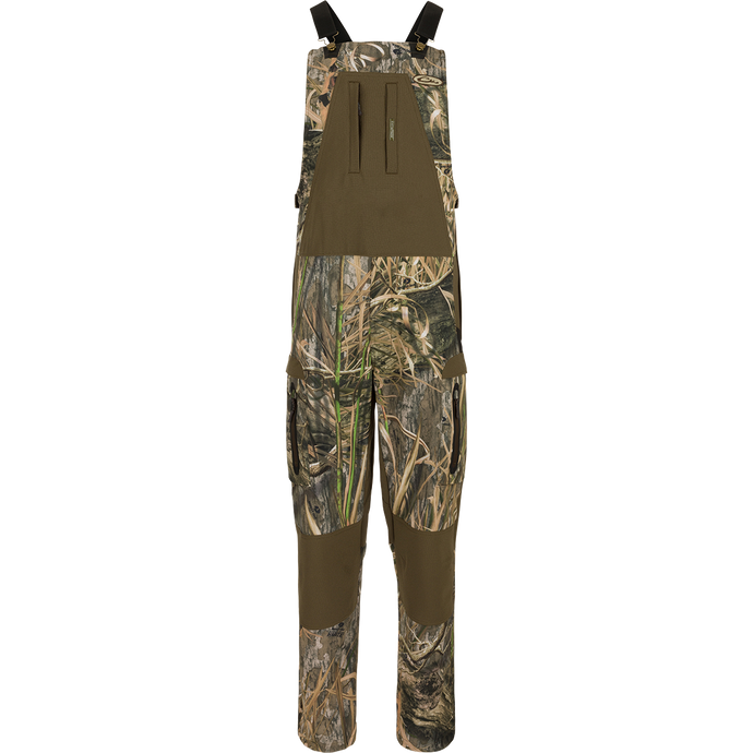 MST Tech Stretch Bibs with camouflage pattern, featuring elastic shoulder straps, multiple zippered pockets, reinforced knees, and silicone inner waistband for hunting versatility.