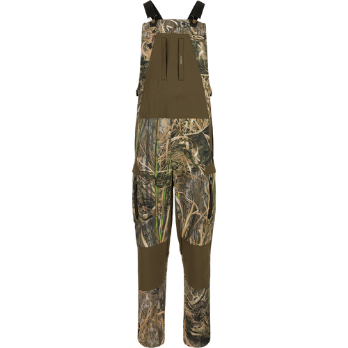 MST Tech Stretch Bibs with camouflage pattern, featuring elastic shoulder straps, multiple zippered pockets, reinforced knees, and silicone inner waistband for hunting versatility.