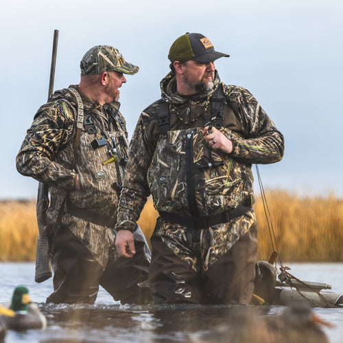 Men in camouflage gear, standing in water, wearing the Technical Performance Fleece Full Zip Jacket, showcasing its outdoor utility in hunting scenarios.