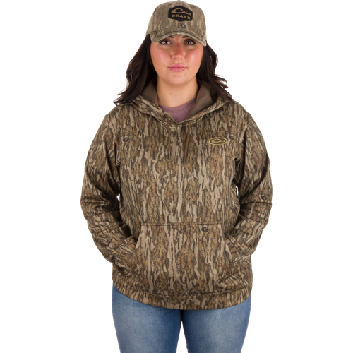 Woman in camouflage hoodie and hat wearing the Women's MST Performance Hoodie, featuring a double-lined hood, kangaroo pouch, and soft, combed fleece interior for warmth and comfort.