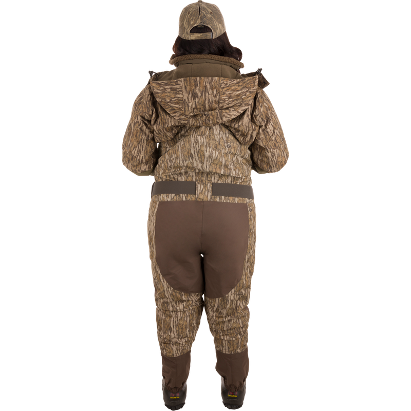 A person wearing Women’s Insulated Guardian Elite Vanguard Breathable Waders with a camouflage pattern, featuring reinforced seams, handwarmer pockets, and Thinsulate Buckshot Mud boots.