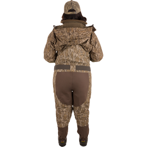A person wearing Women’s Insulated Guardian Elite Vanguard Breathable Waders with a camouflage pattern, featuring reinforced seams, handwarmer pockets, and Thinsulate Buckshot Mud boots.