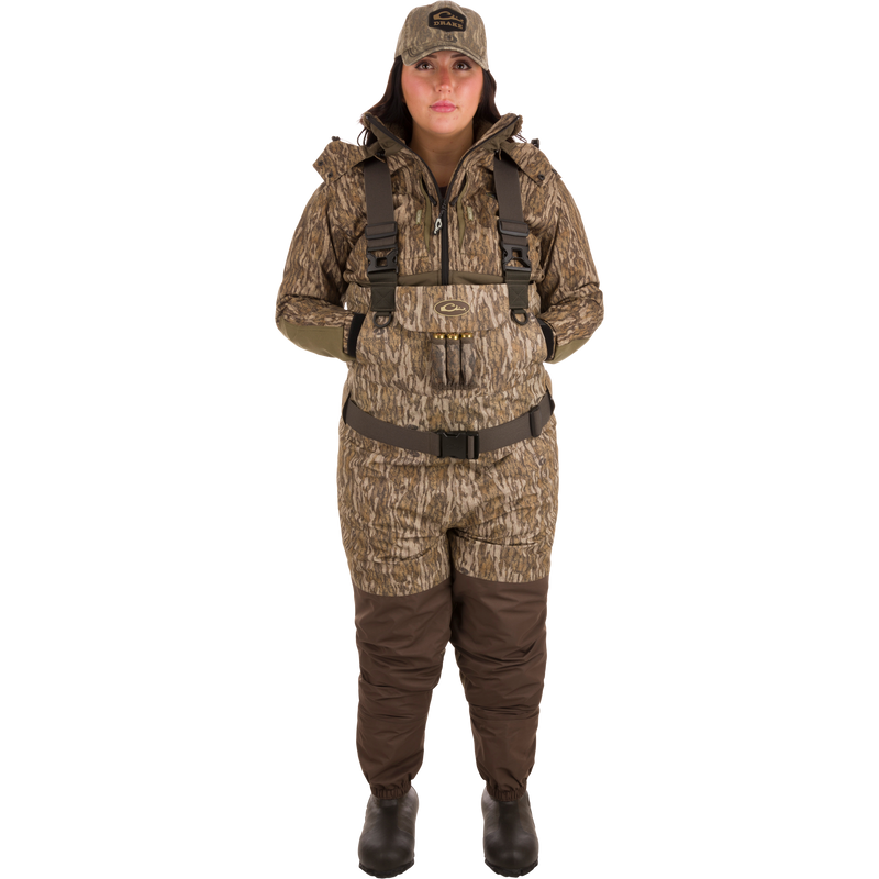 Woman in camouflage Women’s Insulated Guardian Elite Vanguard Breathable Waders, featuring reinforced seams, HD2 material, and multiple pockets for warmth and gear storage.