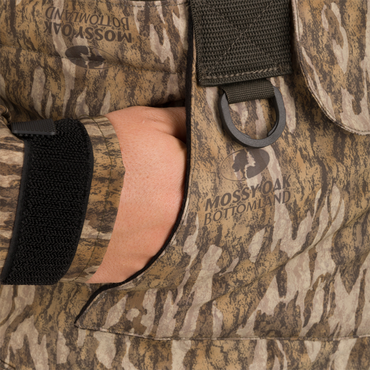 Hand in pocket of Women’s Insulated Guardian Elite Vanguard Breathable Waders, showcasing camo fabric and reinforced seams for durability in harsh hunting conditions.