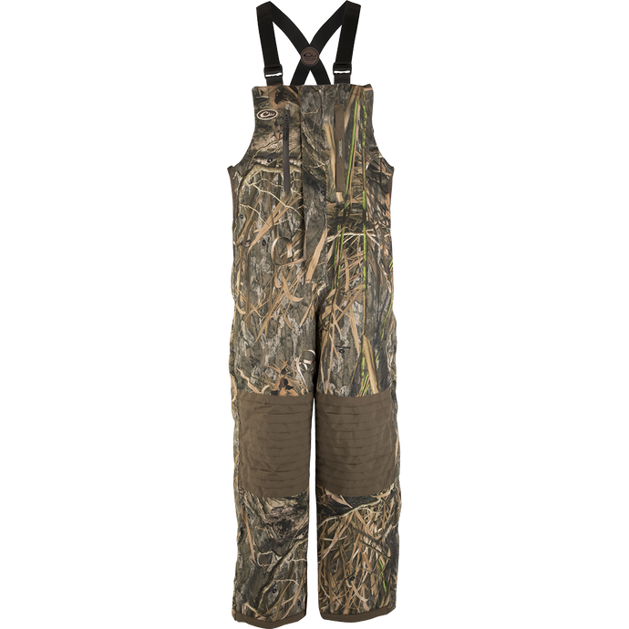 A product image of the EST Guardian Elite™ Bib Shell Weight, featuring a camouflage overall with straps, perfect for hunters seeking protection in all weather conditions. The bib is made of 100% waterproof/windproof/breathable Guardian Elite™ 3-layer pro wader fabric, with reinforced knees, seat, and wear areas. It includes adjustable shoulder straps, Magnattach™ chest pockets, and easy on/off full-length side zippers. Ideal for use in a ground blind.