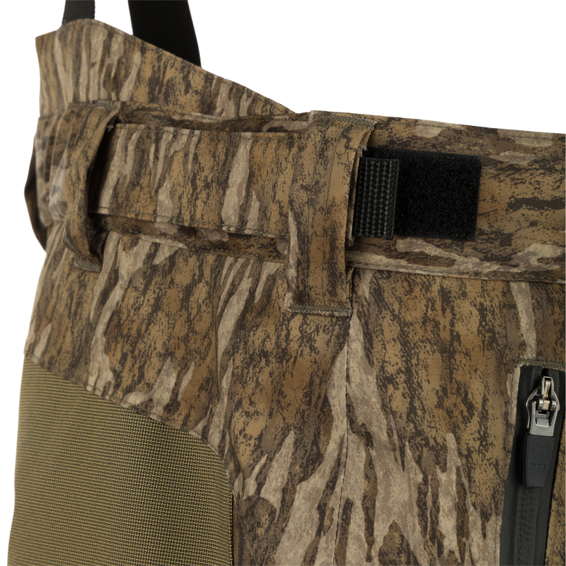 Close-up of MST Waist-High Insulated Bibs showcasing durable zippers, camouflage fabric, and adjustable Velcro waist tabs.