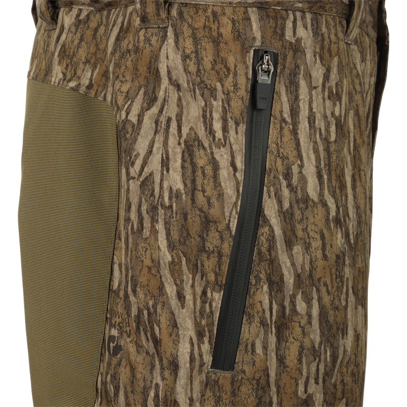 Close-up of MST Waist-High Insulated Bibs featuring camouflage fabric, water-resistant zippers, and adjustable Velcro waist for secure fit.