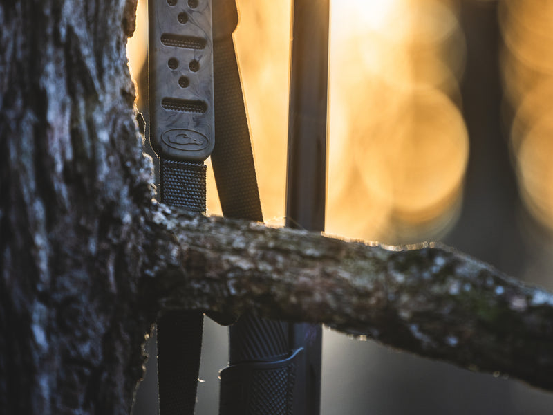 Waterfowl Gunslinger Shotgun Sling securely attached to a tree, showcasing its durable polypropylene braided cord and metal swivel stud connection for reliable shotgun carrying.