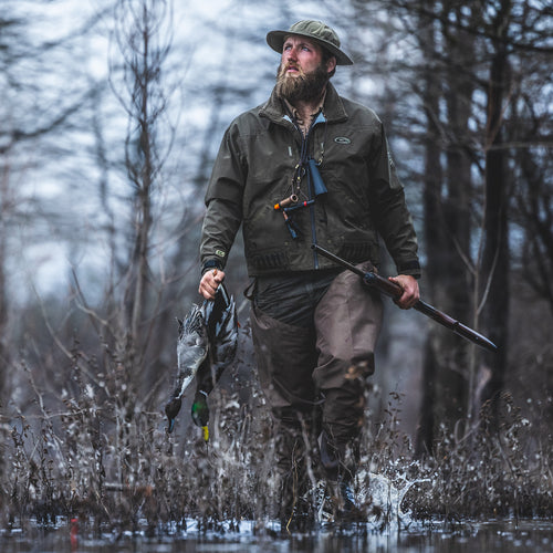 Man in water wearing EST Waterfowlers Hip Boot, holding duck and gun; showcases comfort and mobility in hunting conditions.