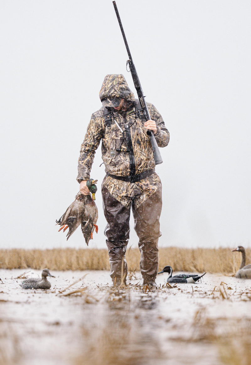 Man in camouflage holding a gun and ducks, wearing an MST Synthetic Down Hooded Jacket designed for warmth and comfort during hunting.