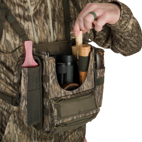 Run-N-Gun Turkey Chest Pack, lightweight and durable, held by person in camouflage. Features multiple pockets, removable bino harness, and stowable rain fly for hunting convenience.