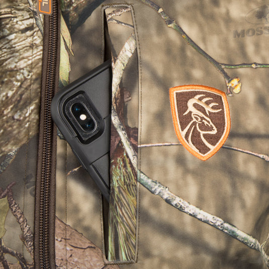 Camo Tech Vest with Agion Active XL: Close-up of a camo vest pocket with a phone, showcasing zipper and scent control technology. Ideal for bow hunting with multiple chest pockets.